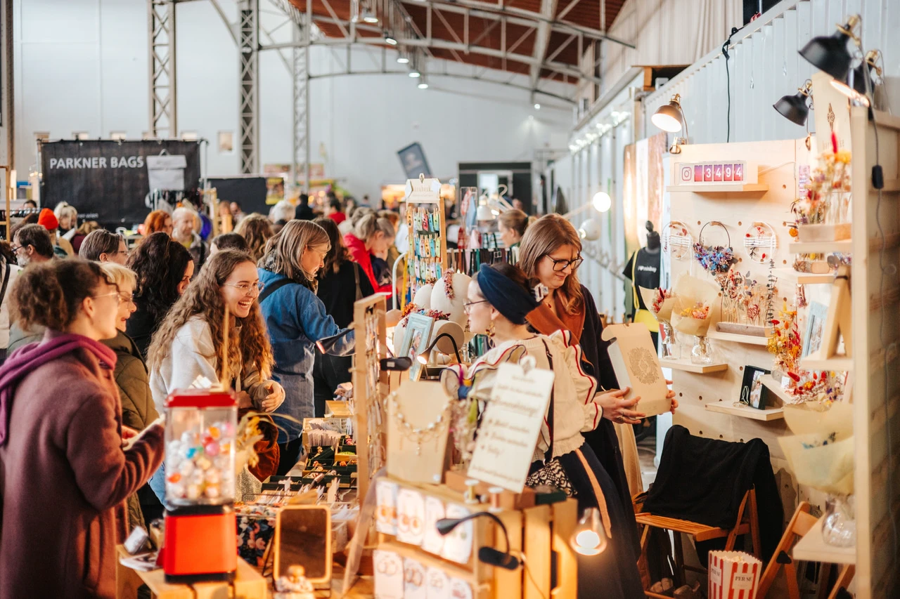 Besucher drängen sich an bunt gestalteten Ständen auf einem lebhaften Handwerks- und Designmarkt in einer großen Halle.